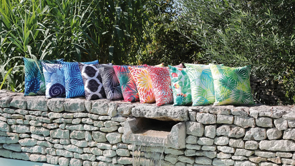 Coussins Proloisirs colorés disposés sur un salon de jardin en résine tressée sur une terrasse ensoleillée